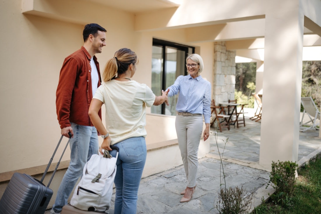 A host greeting arriving guests at the door of a vacation rental.