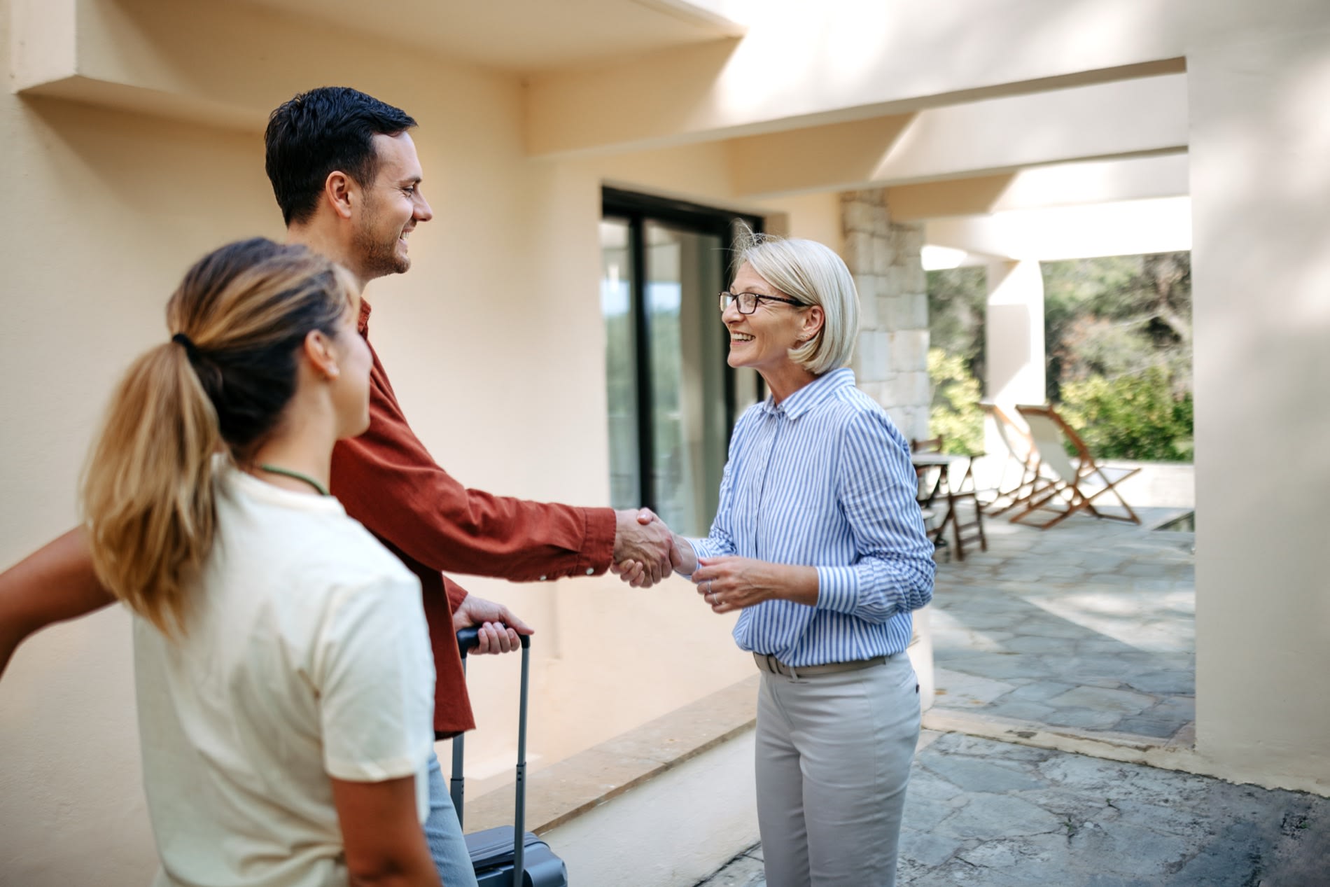 A host greeting arriving guests at the door of a vacation rental.
