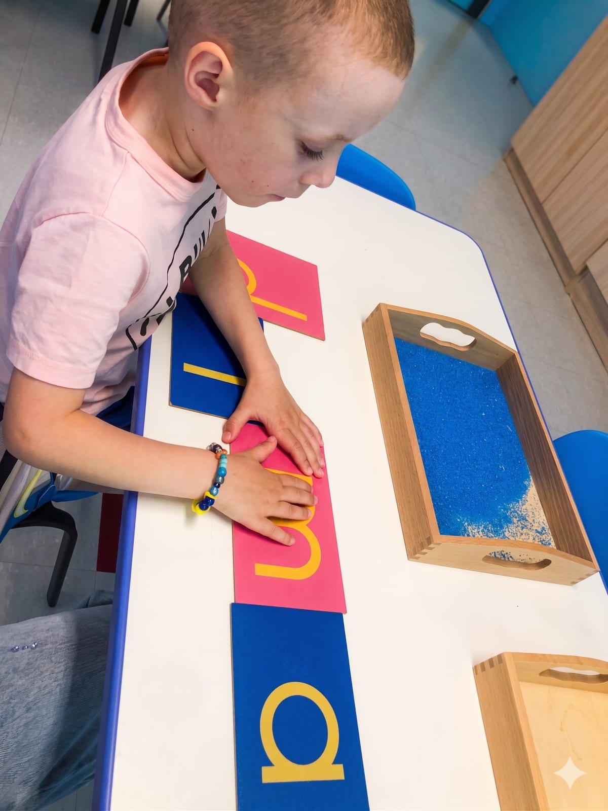 Garderie Ami Câlin, inscriptions petite enfance : un jeune enfant travaille avec le matériel sensoriel Montessori sur la reconnaissance des lettres et l'épellation, dans une atmosphère de classe concentrée. — Garderie Ami Câlin — Photos de classe Montessori — Un environnement Montessori professionnel pour éveiller le plein potentiel de chaque enfant. Inscriptions ouvertes — contactez-nous !