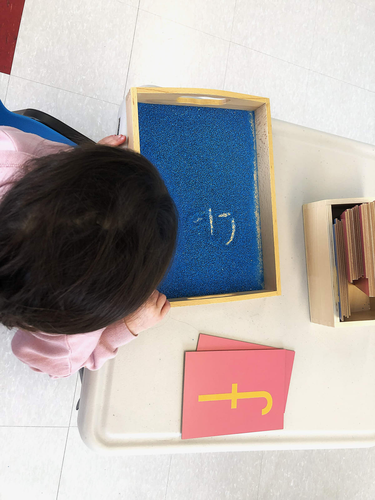 Garderie Ami Câlin, enseignement sensoriel Montessori : un tout-petit trace des lettres dans un bac à sable bleu pour renforcer la mémorisation par le toucher, près de lettres rugueuses. Inscriptions ouvertes à la garderie. — Garderie Ami Câlin — Bac à sable Montessori — Garderie Ami Câlin, Gatineau — inscriptions en cours ; programme Montessori, garde éducative et apprentissage sensoriel.