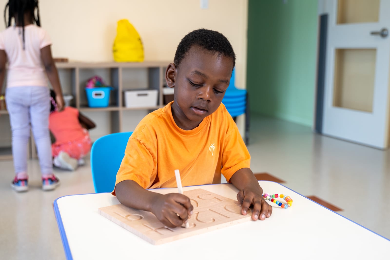 Garderie Ami Câlin : enfant en activité de pré-écriture sur tablette en bois, pour développer le geste graphique, la précision et la confiance.