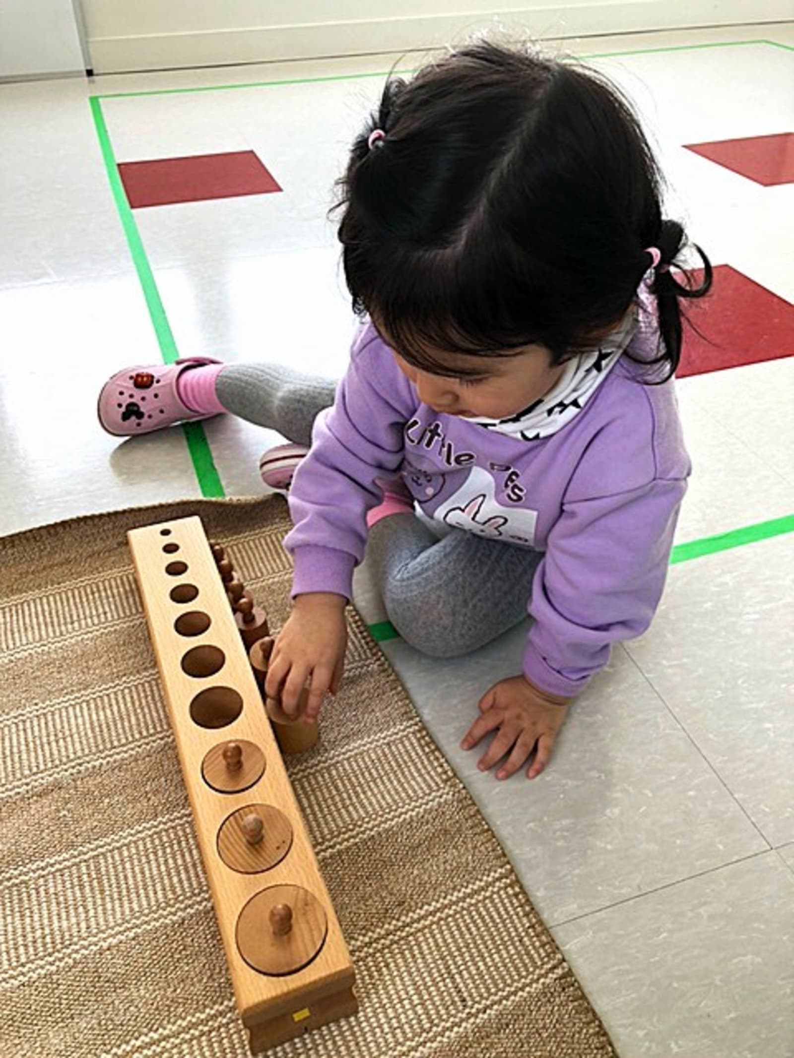 Garderie Ami Câlin — atelier Montessori en petite enfance : un enfant manipule les blocs de cylindres pour distinguer tailles et dimensions, et développer concentration et sens de l'observation. Inscriptions en cours. — Garderie Ami Câlin — Exercice Montessori avec blocs de cylindres — Mots-clés : Garderie Ami Câlin, matériel Montessori, blocs de cylindres, inscriptions, entraînement sensoriel.