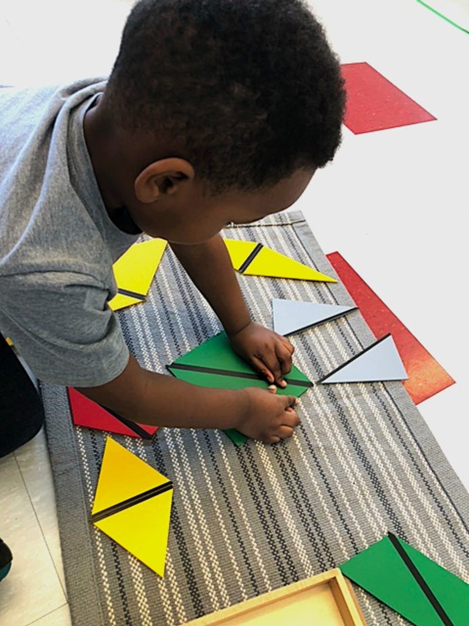 Garderie Ami Câlin — activité Montessori de géométrie et motricité fine : un enfant manipule des formes colorées, vu du dessus, pour développer la perception de l'espace. Environnement de garde éducative professionnel. Inscriptions ouvertes. — Garderie Ami Câlin — Activité géométrique et motricité fine — Atelier géométrique Montessori: manipulation des formes, concentration et structuration de l'espace.