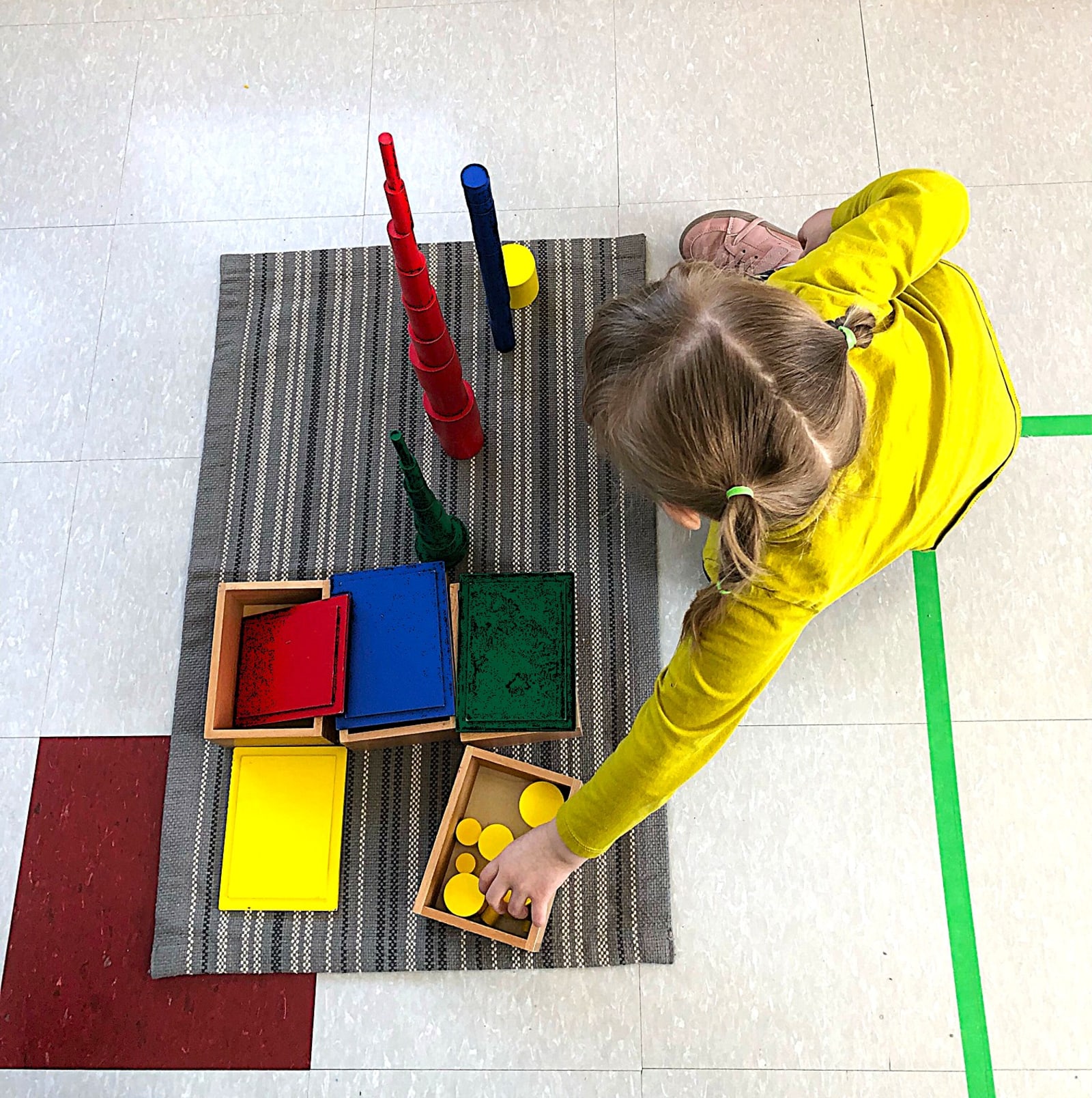 Garderie Ami Câlin — activité sensorielle Montessori : un enfant, vu du dessus, empile et classe des cylindres colorés. Un environnement professionnel de garde éducative à la petite enfance. Inscriptions ouvertes. — Garderie Ami Câlin — Activité sensorielle et motricité fine — Atelier sensoriel Montessori: tri, empilement et motricité fine dans un environnement éducatif professionnel.