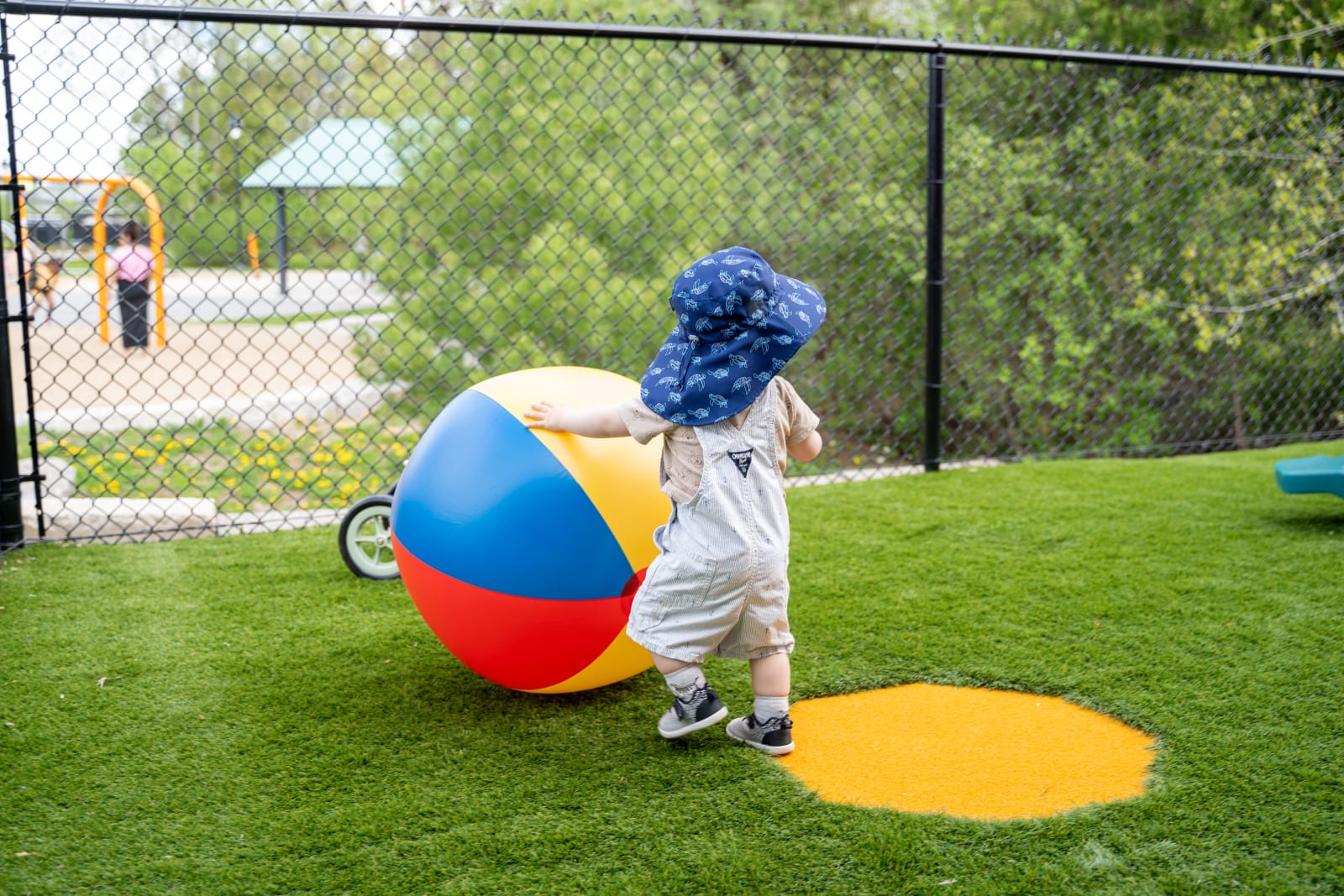 Moment d'activité extérieure à Garderie Ami Câlin : un tout-petit joue avec un grand ballon sur une aire de jeu en gazon synthétique sécuritaire, pour développer l'équilibre et la motricité globale. L'image met en valeur la qualité de l'environnement pédagogique extérieur de notre garderie à Gatineau. — Garderie Ami Câlin — Activité extérieure et développement de la littératie physique — Mots-clés : Garderie Ami Câlin, aire de jeu extérieure, littératie physique, activité motrice préscolaire, garderie Gatineau, inscriptions.