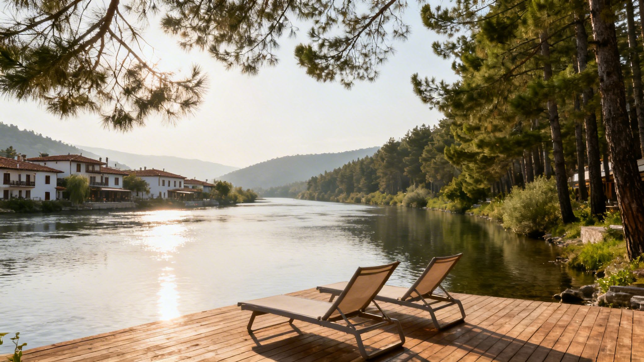 A tranquil river scene with sun loungers on a wooden deck, a village, and a forest.