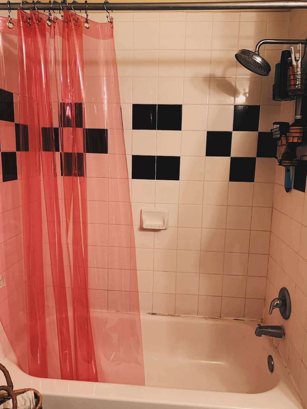 after shot of the shower with a hanging, brass shower organizer and a bright pink transluscent shower curtain