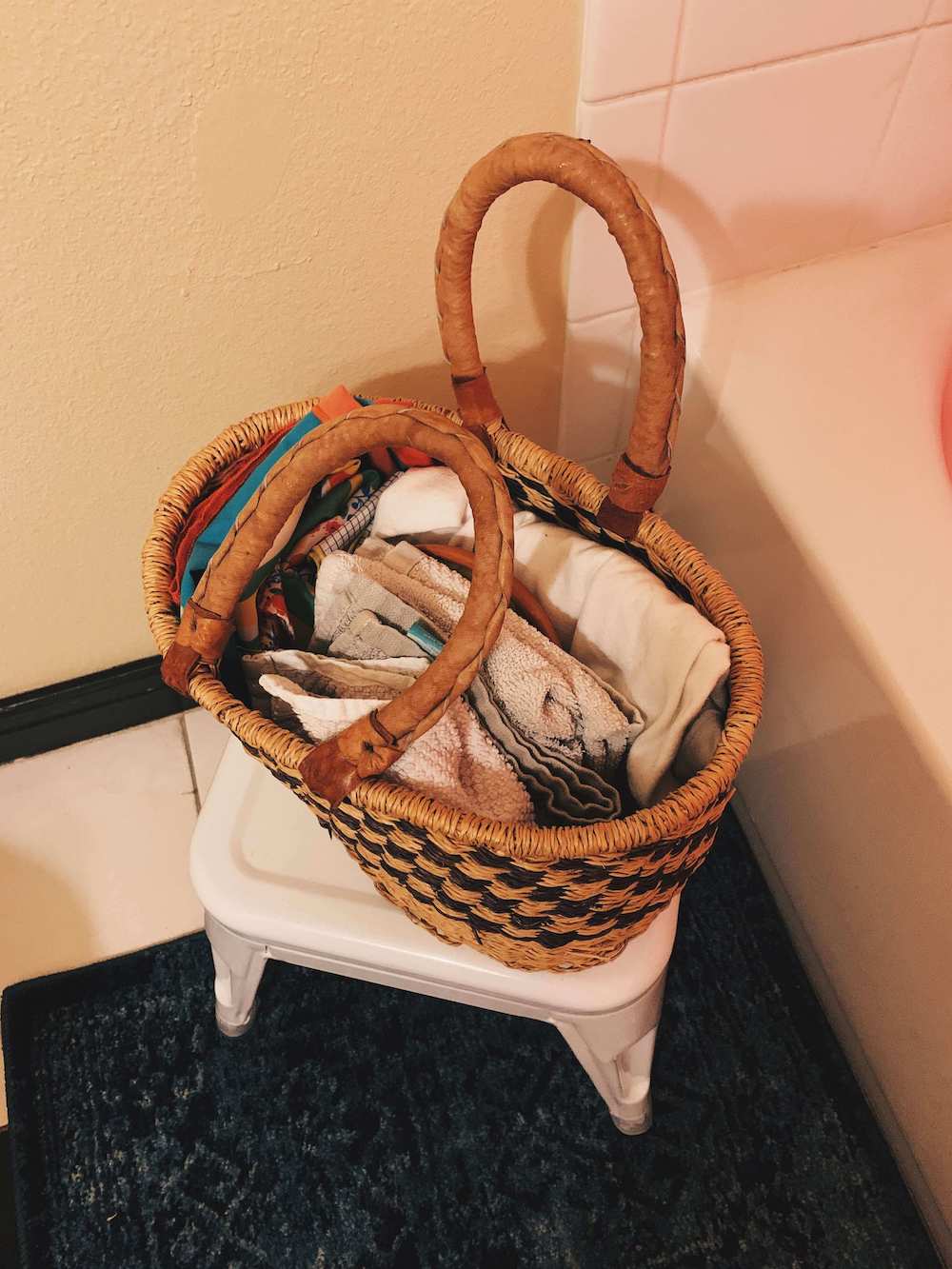 after shot of wicker basket on a white stool. the basket stores folded washcloths.