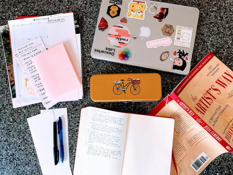 flat lay of laptop, notebook, and the Artist's Way book on a counter