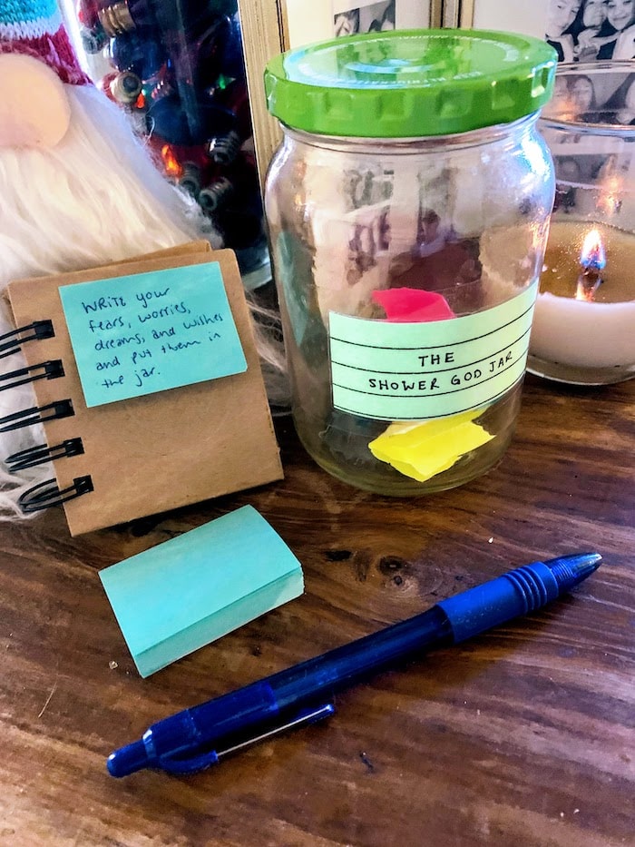 a glass jar labeled "the shower god jar" with post it notes and pen for writing your fears and dreams