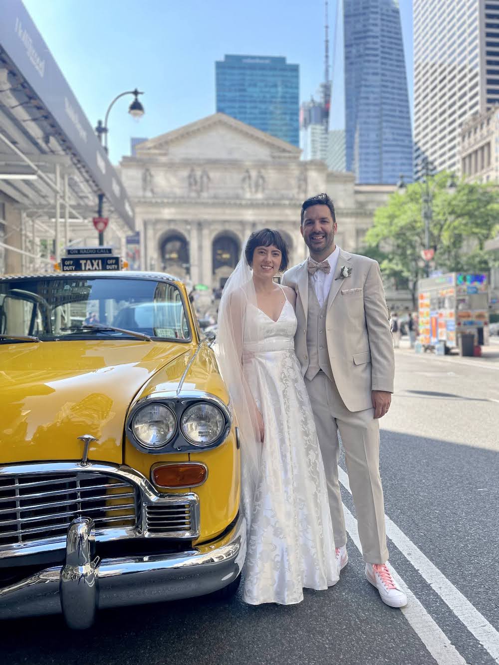 bride and groom in front of a vintage yellow cab with the New York Public Library in the background