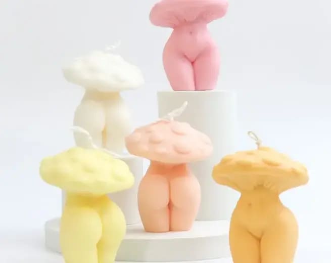 Pink, orange, yellow, white, and peach colored candles, desgined to have the bottom half of a woman's nude torso to thigh, and the top half a mushroom head.