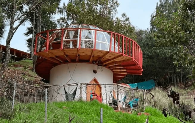 An airbnb home with a dome roof and round balcony nestled in the forest.