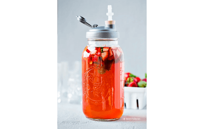 A mason jar full of strawberry-mint kombucha inside, with bits of strawberries and mint.