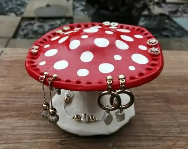 Sculpture of a red mushroom with white polka dots with holes in the top to hang earrings.