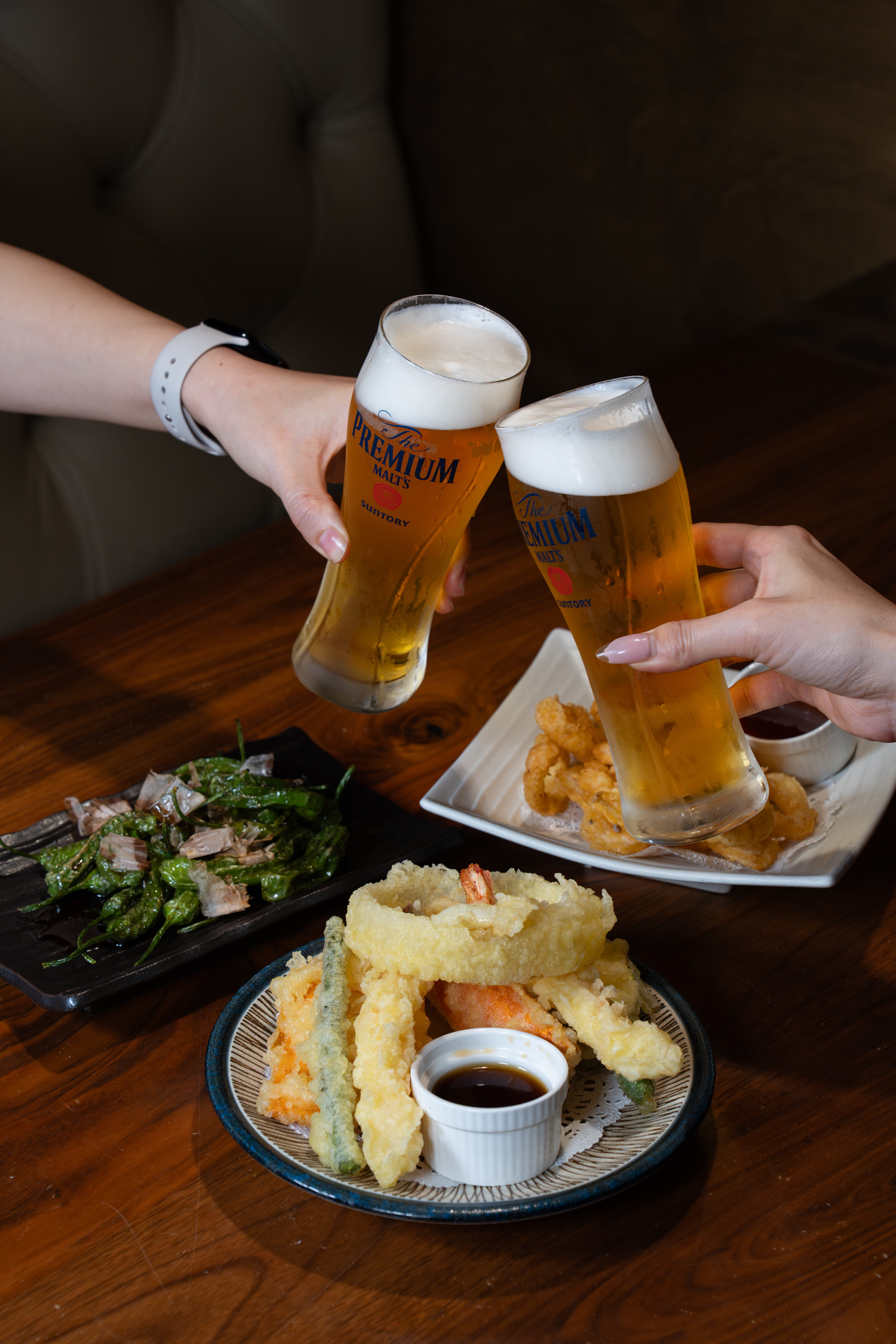 Two glasses of Japanese beer alongside appetizer plates featuring edamame and gyoza at Yume Long Beach