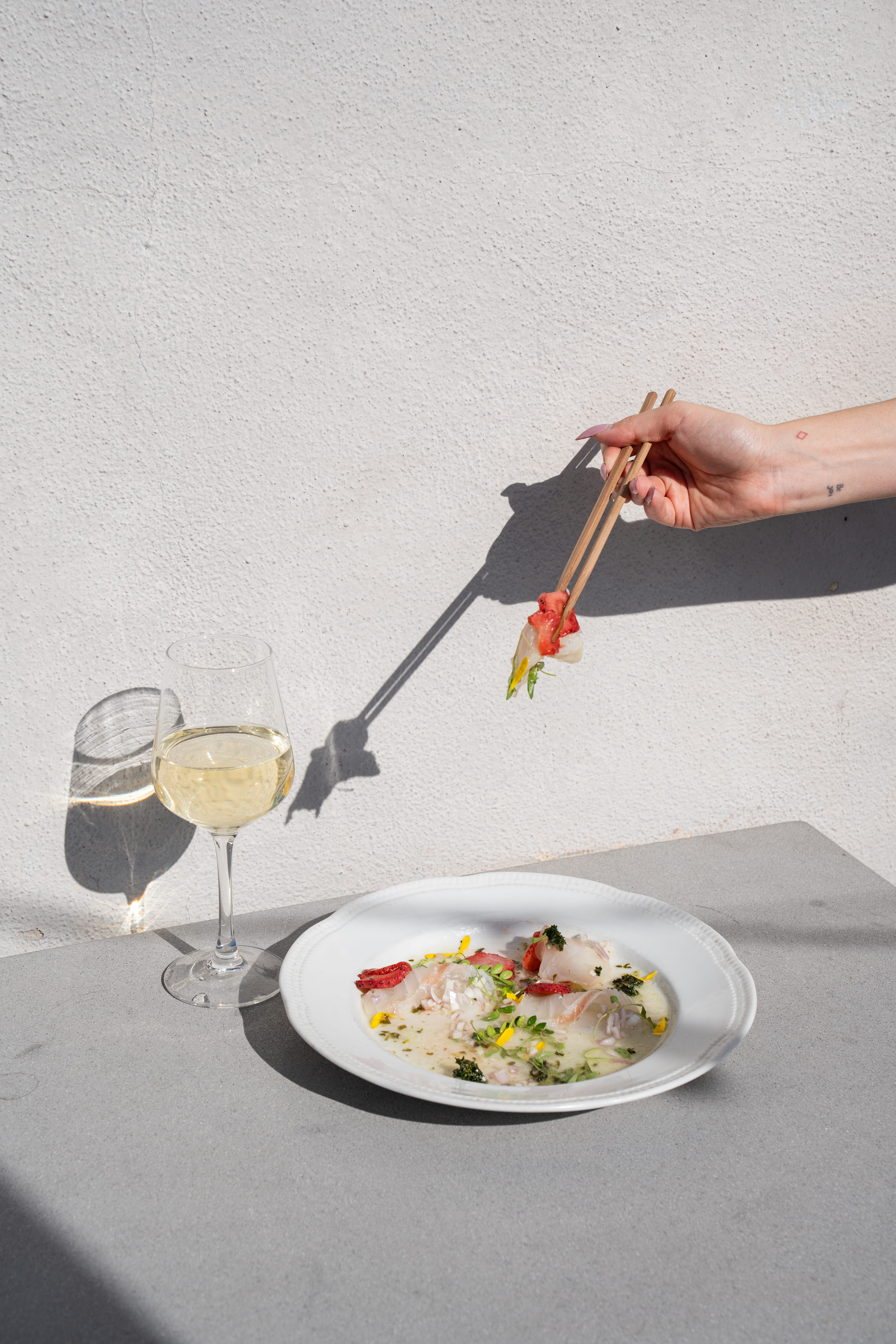 A glass of white wine paired with a fresh sashimi platter featuring salmon, tuna, and yellowtail at Yume Manhattan Beach