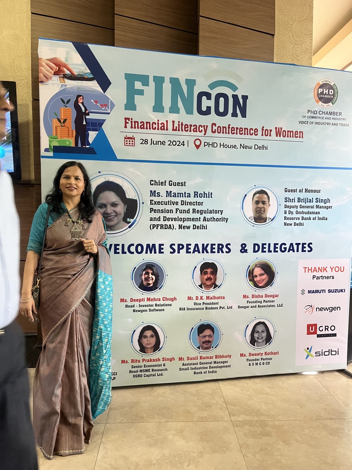 CA Sweety Kothari standing in front of the FINCON Financial Literacy Conference for Women banner, which lists her among the welcome speakers.