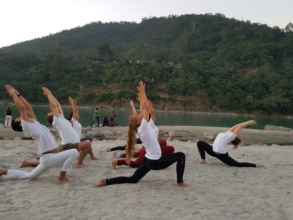 Yoga student practicing asana on the banks of the Ganga River with the Himalayan foothills in the background, Rishikesh yoga