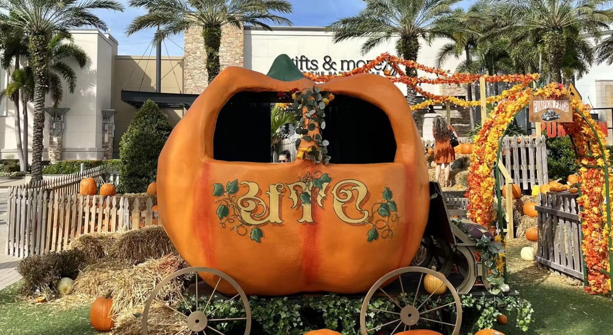 A giant pumpkin carriage with "UTC" painted on the side, surrounded by hay bales and pumpkins at the UTC pumpkin patch
