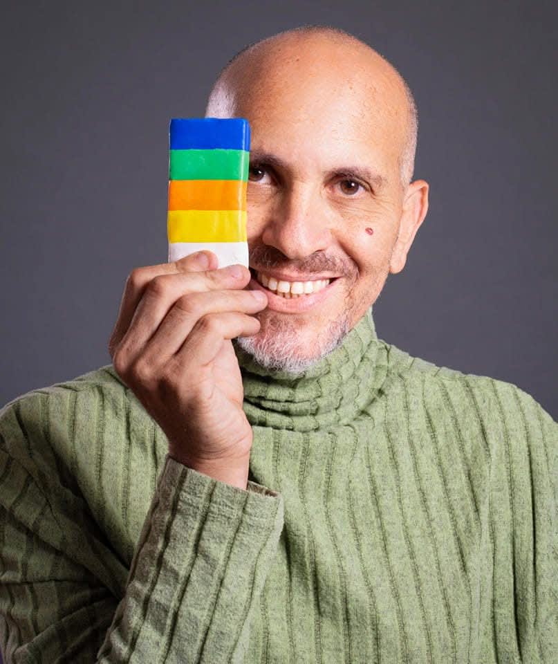 שניר פלג, מדריך סדנאות פלסטלינה, מחייך למצלמה בסטודיו יצירה עם יצירות פלסטלינה ברקע.