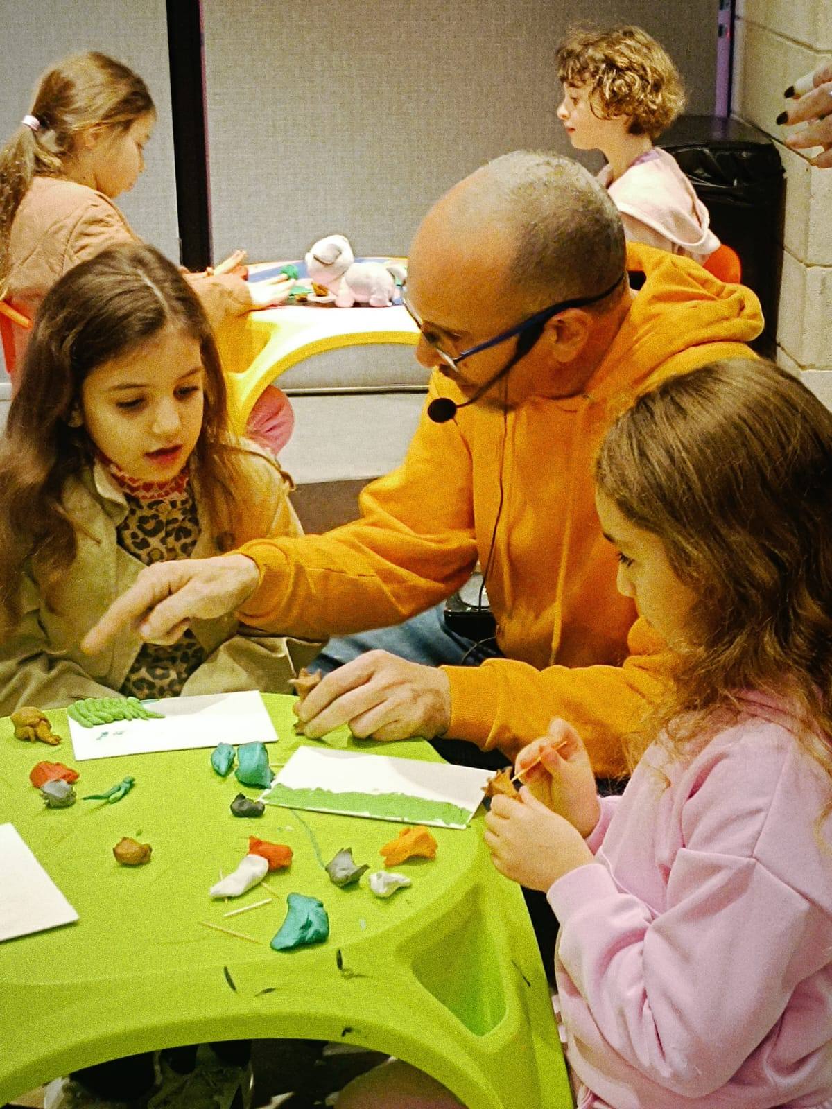 ילדה צעירה מציגה בגאווה את יצירת הפלסטלינה שלה: דמות של איש שלג עם כובע וצעיף.