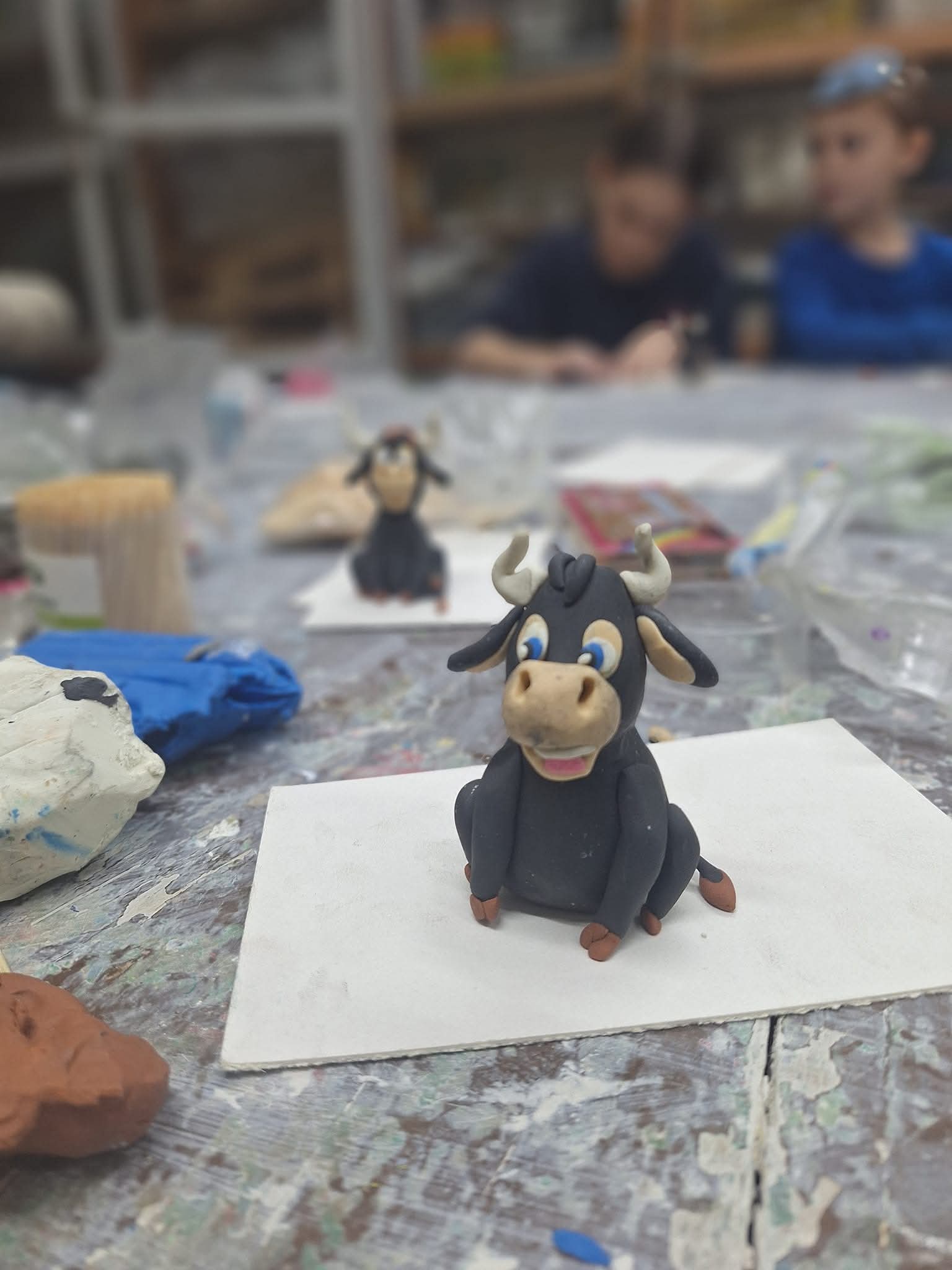 ינשוף קטן וחמוד עשוי פלסטלינה כתומה, עומד על ענף דק, תוצר של סדנת ילדים.