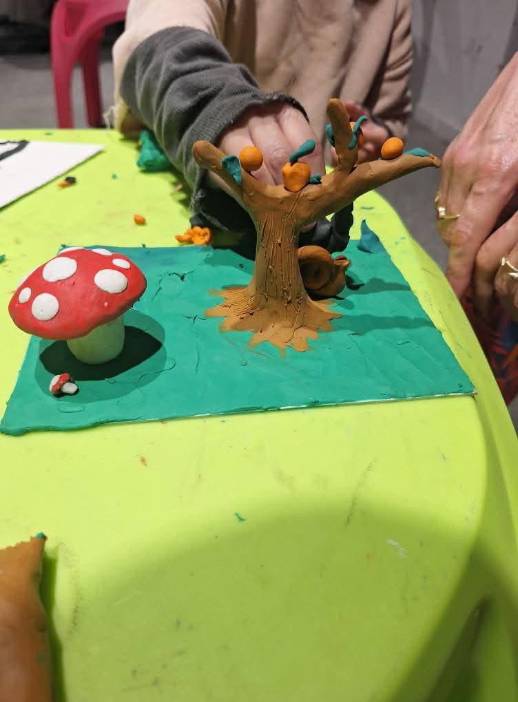 סצנה שלמה מפוסלת בפלסטלינה: בית קטן עם גינה ודמויות, המציגה סיפור ויזואלי.