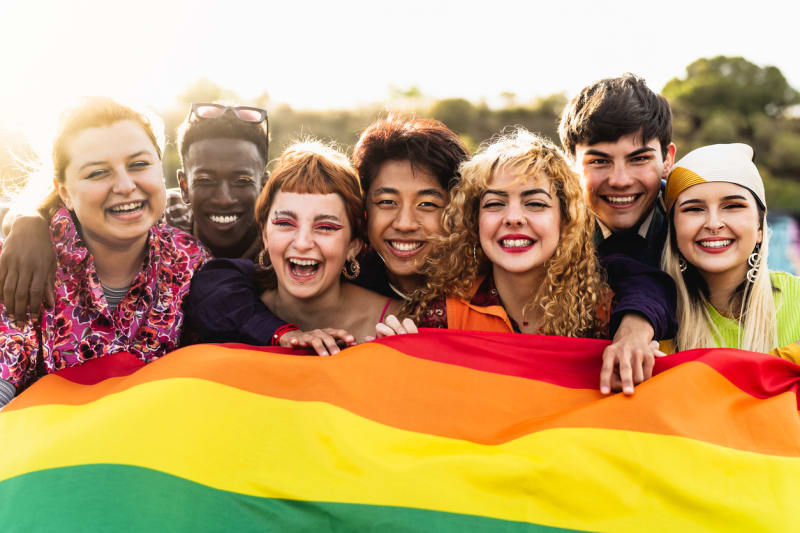 Young people smiling together holding a rainbow flag