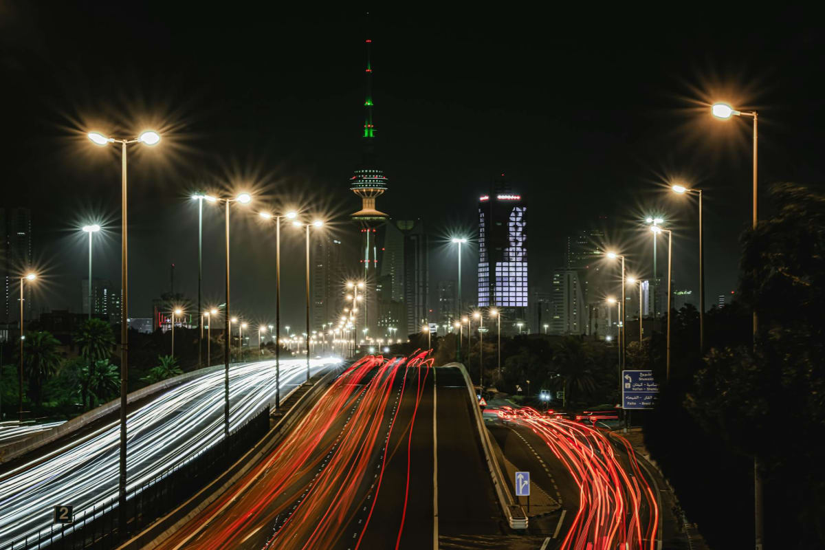 Vibrant light trails and illuminated skyline of Kuwait City at night, highlighting urban life.