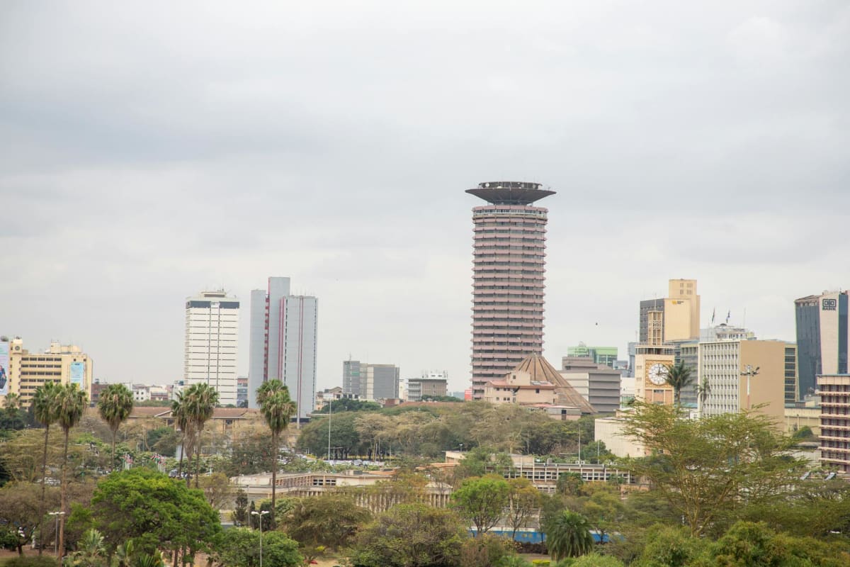 View of Nairobi's skyline with the iconic KICC tower and surrounding high rises under a cloudy sky.