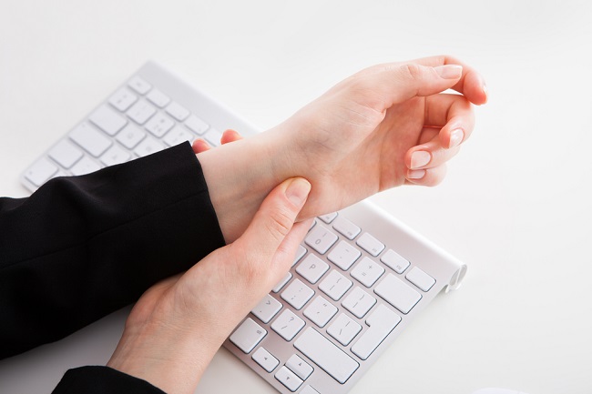 Cropped image of businesswoman suffering from wrist pain with computer keyboard on office desk