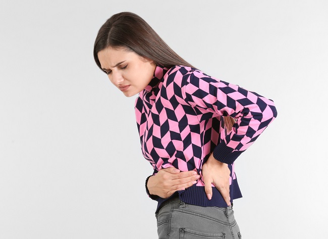 Young woman suffering from flank pain on light background
