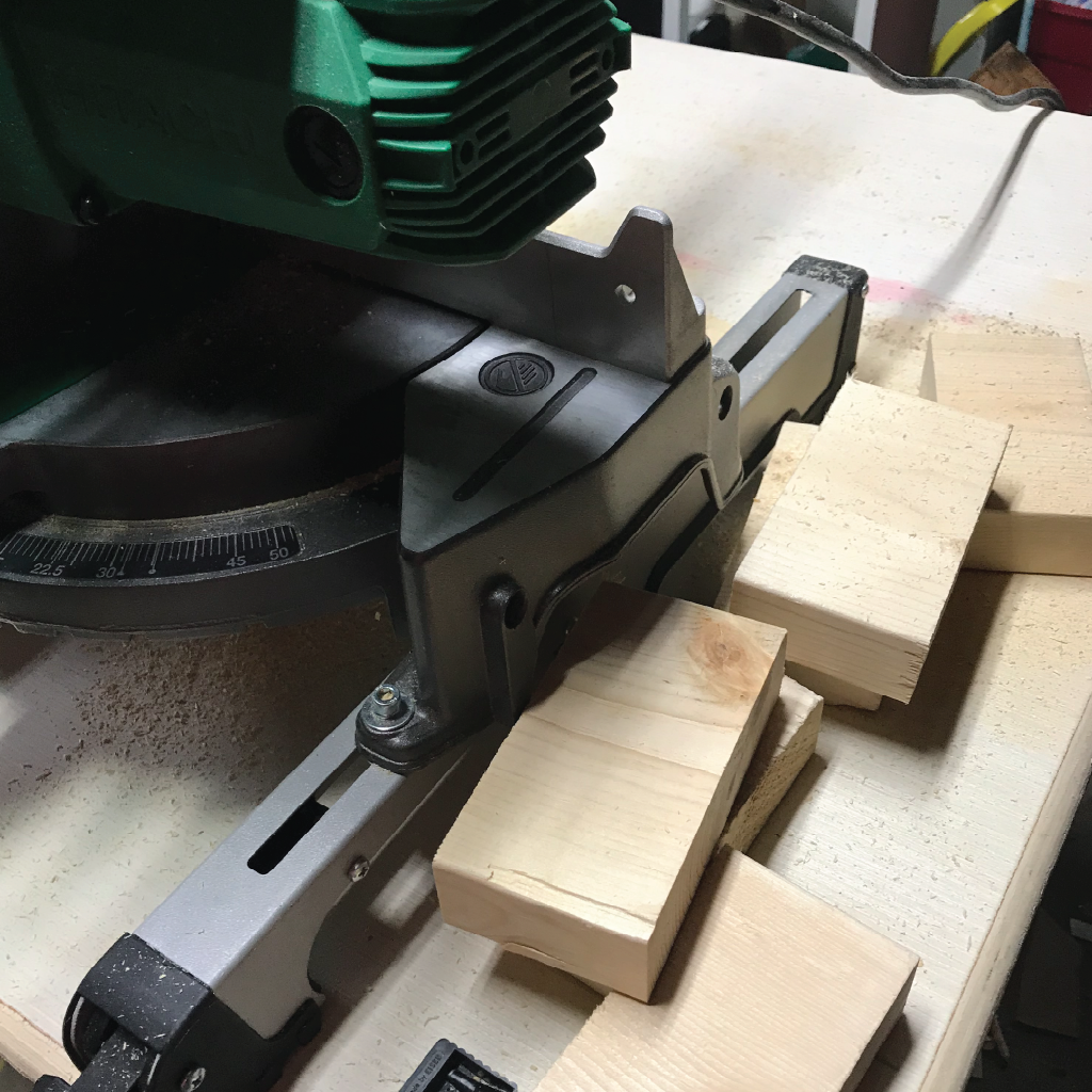 Two inch blocks sitting beside a miter saw that have been cut from the ends of two by sixes