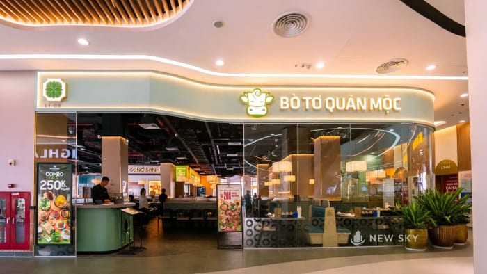 Gian Bò Tơ Quán Mộc trong trung tâm thương mại Vincom Mega Mall Royal Island: dải biển chữ nổi cong theo mặt dựng, nửa gian mở thẳng ra lối đi và nửa kia là vách kính.