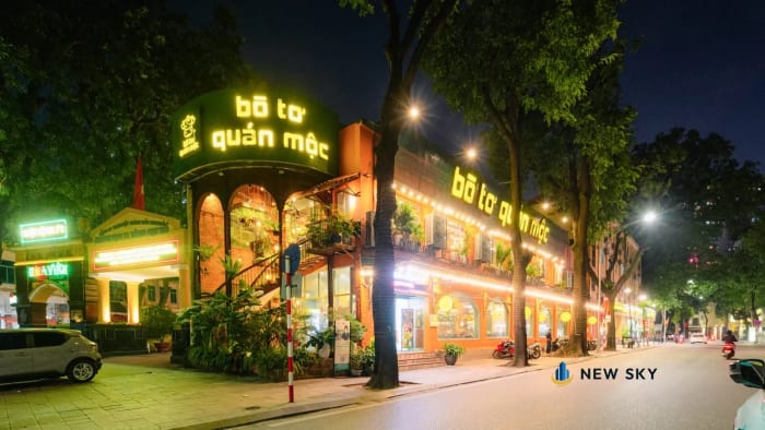 Mặt tiền Bò Tơ Quán Mộc số 1 Tăng Bạt Hổ: biển chữ đèn trên khối tháp góc và dải chữ chạy dọc mặt phố bên, sau hàng cây vỉa hè.