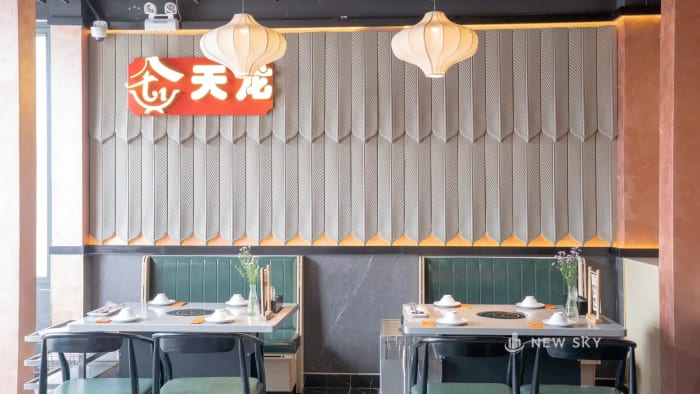 Phòng ăn với vách đắp phù điêu gờ nổi chạy dọc, trần đen để hở kết cấu, và hai dãy ghế băng bọc đệm kê sát vách.