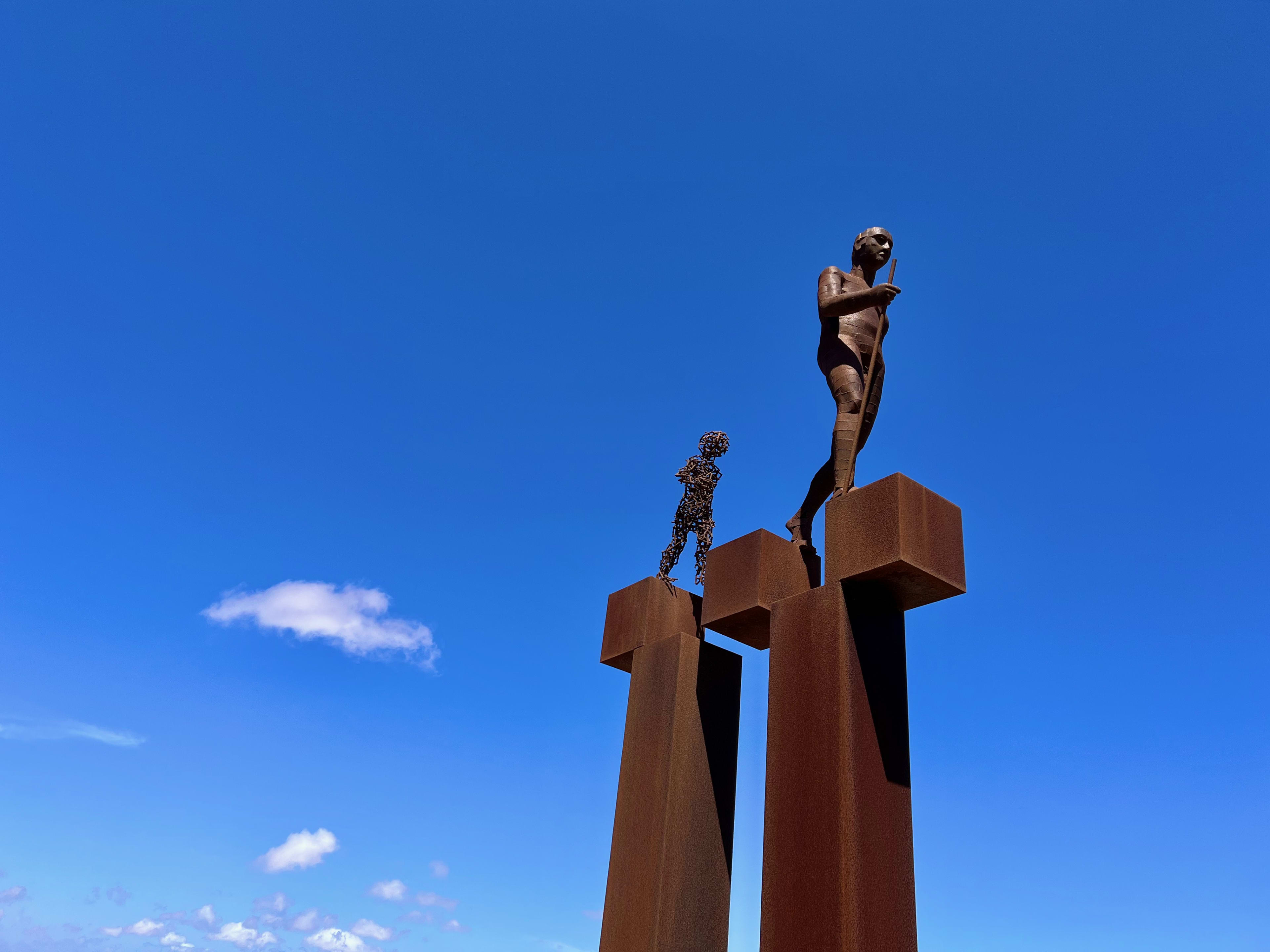 Photograph of statues against a bright blue sky.