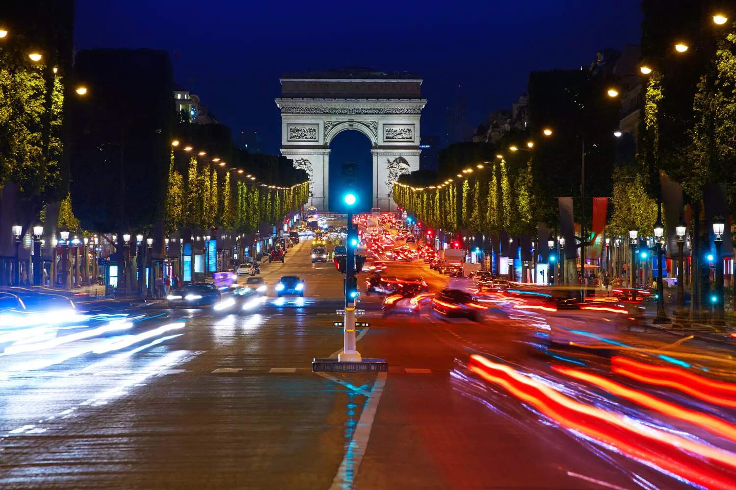 Vue de nuit de l'Arc de Triomphe avec trafic dense sur les Champs-Élysées, service de chauffeur privé Lux Ride Paris