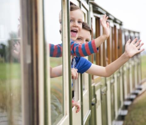 Two children waving at the camera out the window of a train.