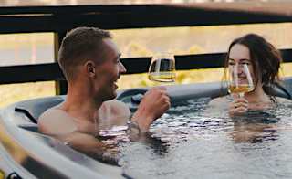 A couple in the hot tub at our stunning Cornish park, Retallack Resort. The male and female are enjoying a glass of wine together. image