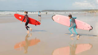 Two children running on the beach with surf boards towards the sea.