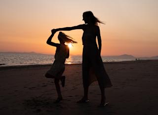 A mother and daughter dancing on the beach at sunset. image