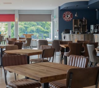 The seating area at The View Bar & Coffee Lounge at our Dorset holiday park, Swanage Bay View. There are tables and chairs and a view of the bar and Costco Coffee sign in the background. image