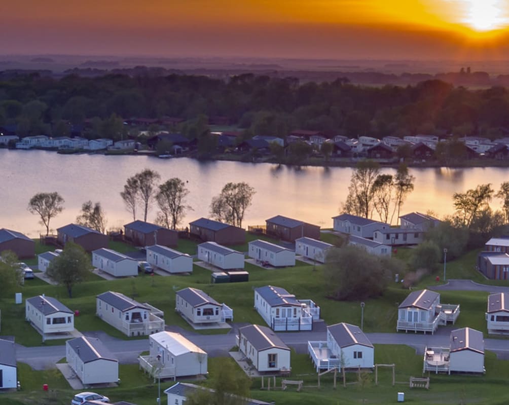 An arieal photoof a holiday park at Tattershall Lake, Lincolnshire. The sun is setting over the horizon and the park has holiday lodges in neat rows by the river.
