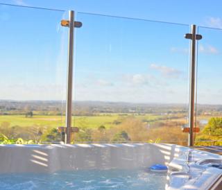 A closeup photo of an outdoor hot tub next to glass fencing on a bright sunny day at out holiday park in Sandy Balls, Hampshire.