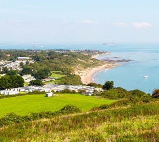 A view of our Whitecliff Bay holiday park. The cliffs are overlooking the sea, with boats cruising around. The coastline stretches far into the distance. image