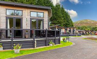 A view of the exterior of our stunning holiday homes for sale at Glendevon Residential Country Park, Scotland. There is a row of wooden lodges and views in the background of the stunning surrounding scenery. image
