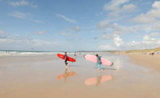 Two children running on the beach with surf boards towards the sea. image