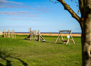 The outdoor adventure playground at our Essex holiday park, Mersea Island, on a sunny day with views of the sea in the background. image